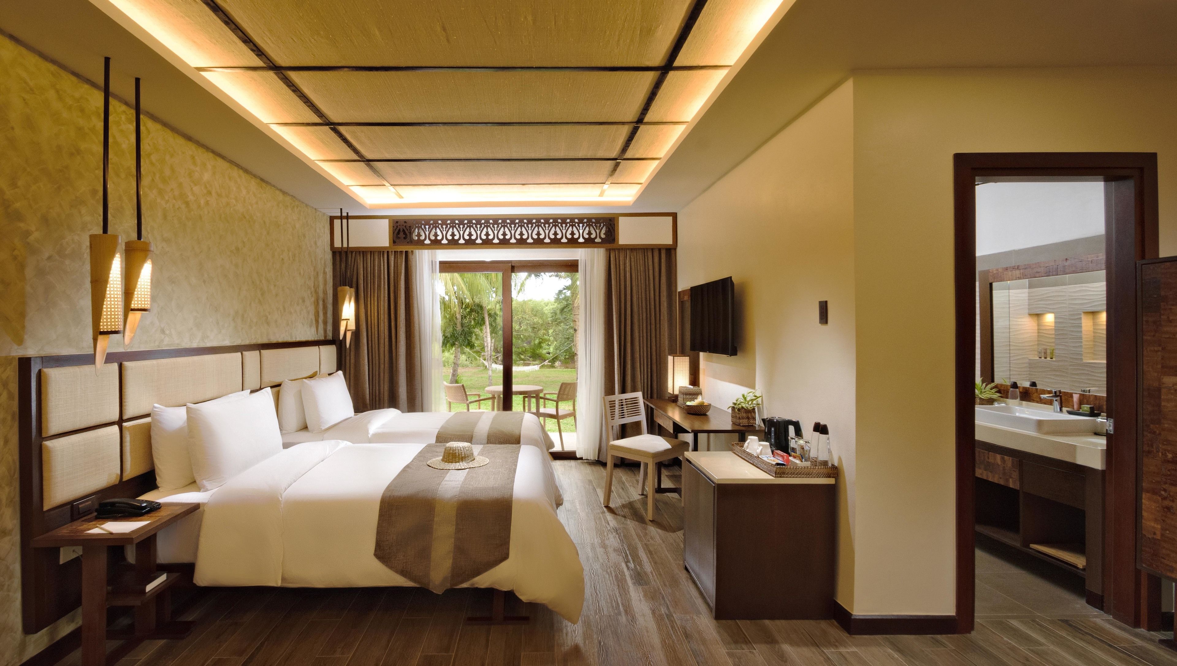 A hotel room with a large bed, a desk, a chair, a TV, and a bathroom visible through an open door.