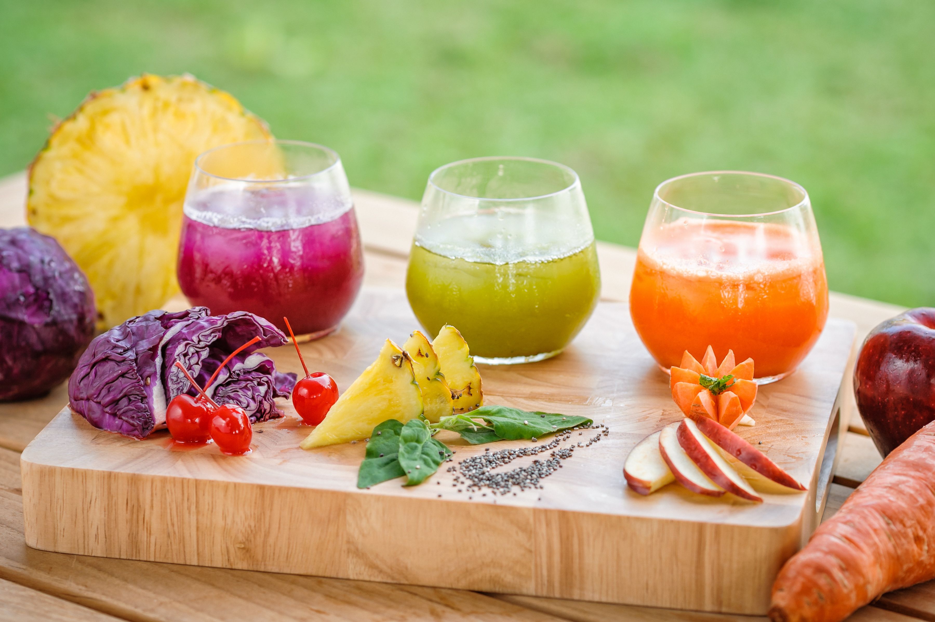 A wooden board with various fruits and vegetables, including a pineapple, red cabbage, cherries, and a carrot.