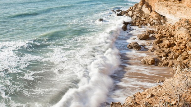 A coastal landscape with a rocky shoreline and waves crashing onto the beach.