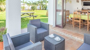 A patio area with wicker furniture, a table with plates, and a view of a grassy yard with trees.