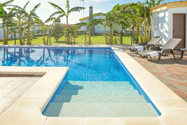 A swimming pool with clear water, surrounded by a tiled deck, and equipped with sun loungers.