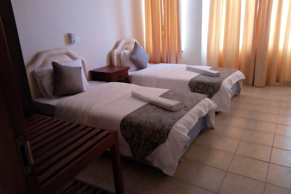Une chambre d’hôtel avec deux lits, un banc en bois et une table de chevet.