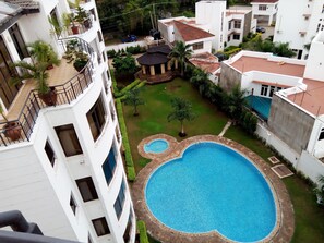 A residential area with a large swimming pool surrounded by a stone border, a small garden with a gazebo, and a white building with balconies. - Impala Apartments Nyali (Mombasa)