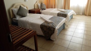 Habitación de hotel con dos camas, una silla de madera y una mesita de noche.