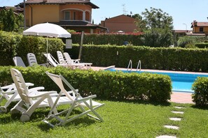 A pool area with lounge chairs and an umbrella, surrounded by well-maintained hedges and a clear blue pool.