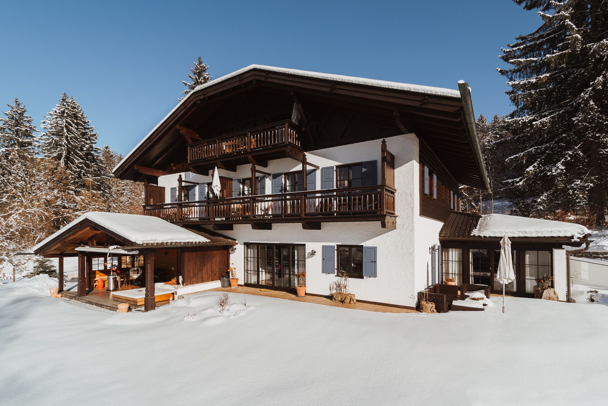 Eine zweistöckige Chalet mit Holzbalkon, großen Fenstern und einem mit Schnee bedeckten Dach.