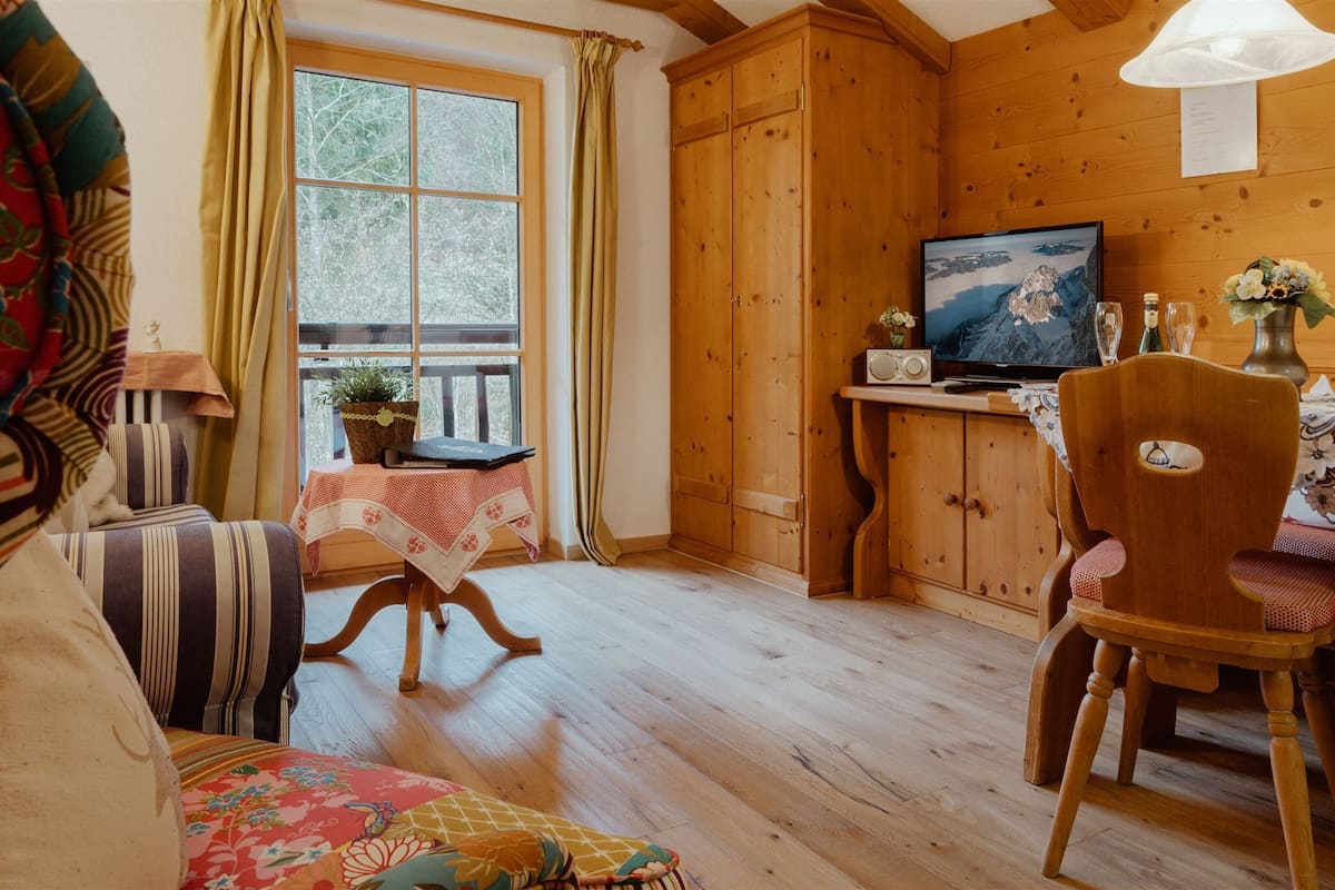 Um quarto aconchegante com piso de madeira, televisão, mesa de jantar com cadeiras e uma janela com cortinas.