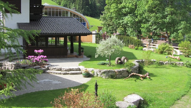 A traditional chalet with a curved roof, surrounded by a well-maintained garden with stone pathways and a variety of plants. - Ferienhaus Heimhof (Garmisch-Partenkirchen)