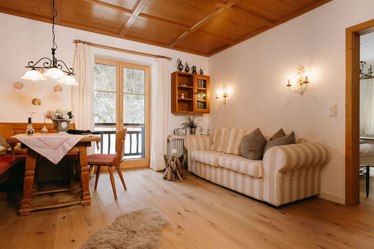 Uma sala de estar aconchegante com teto de madeira, sofá listrado, mesa de jantar com toalha branca e um armário de madeira com objetos decorativos.
