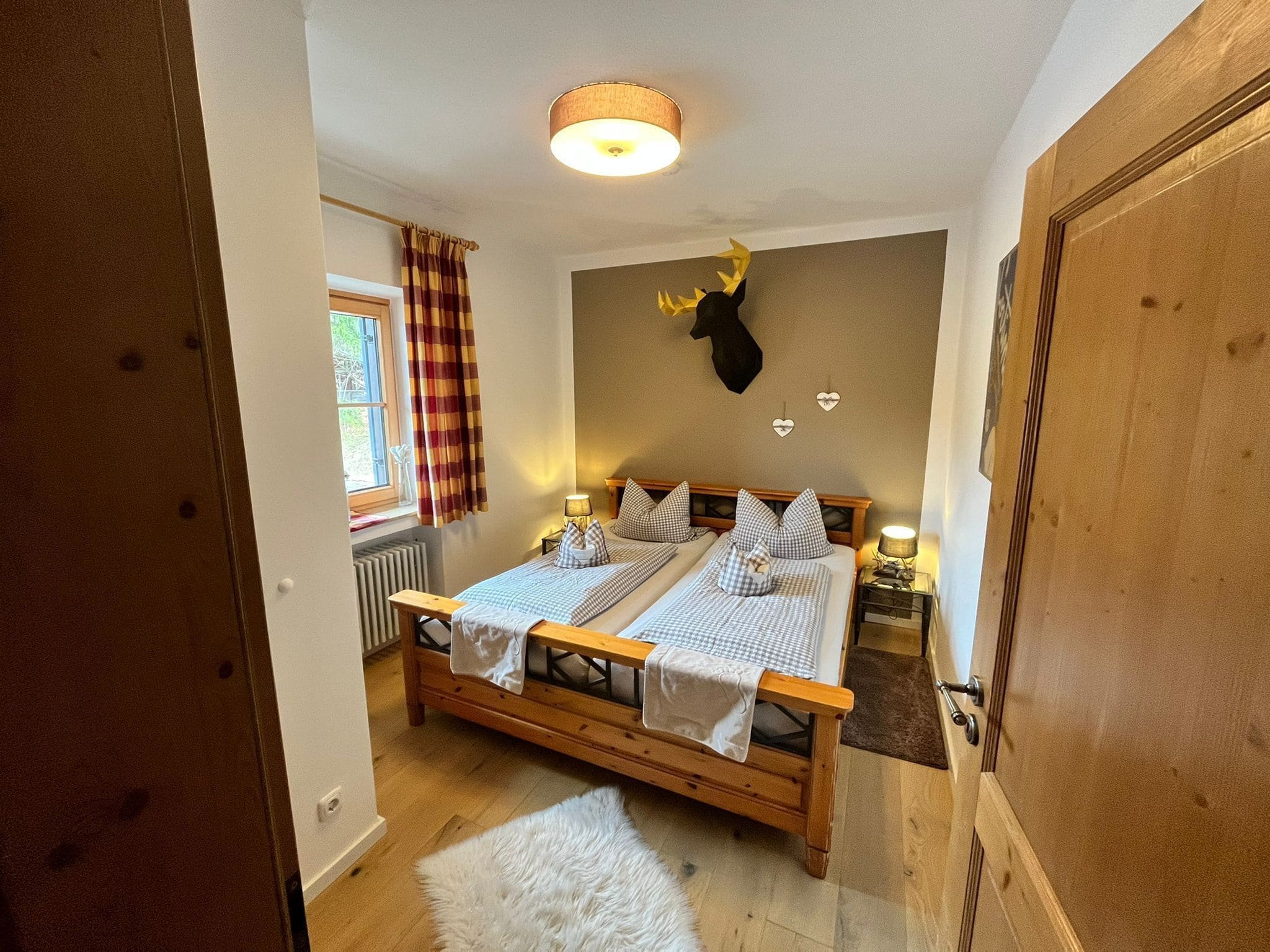 A bedroom with a double bed, a mounted deer head, a window with curtains, and a radiator.