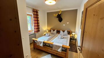 A bedroom with a double bed, a mounted deer head, a window with curtains, and a radiator.
