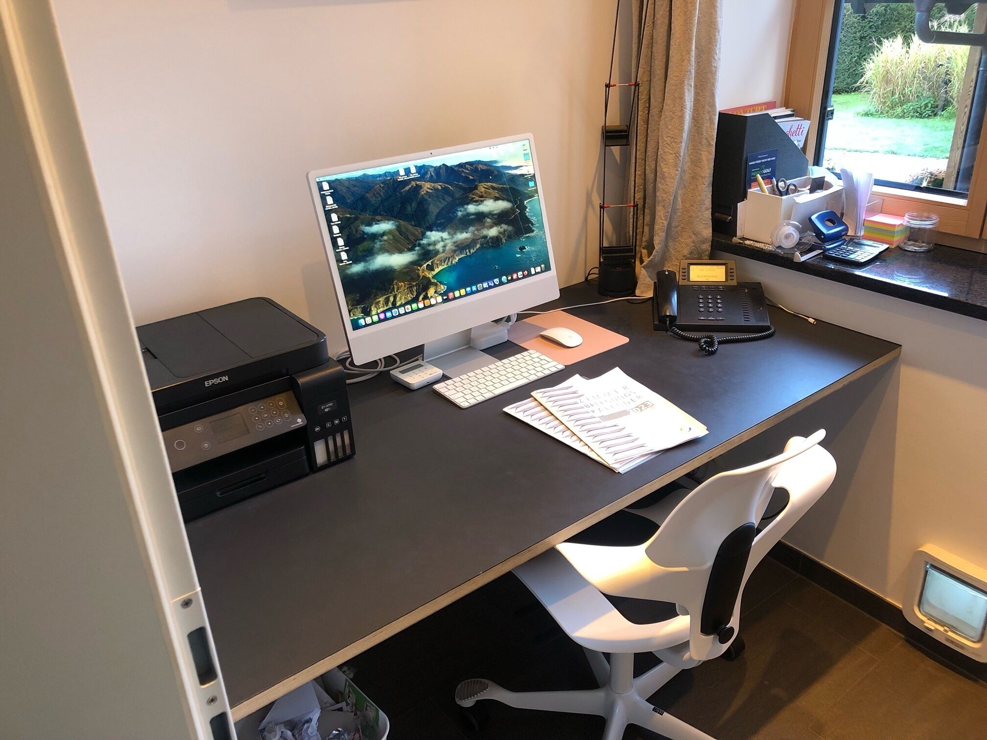 Ein moderner Schreibtisch mit einem Desktop-Computer, Drucker und Telefon.
