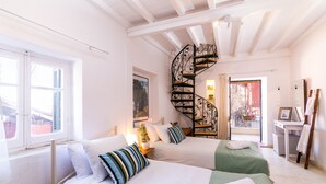 A hotel room with two beds, a spiral staircase, a desk with a chair, and a window with a view of the outside. - Nina's Traditional House by Estia (Corfu)