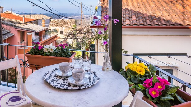A balcony with a round table, chairs, and potted plants. - Nina's Traditional House by Estia (Corfu)