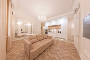 Relax in a spacious living room with a plush sofa, chandelier, and modern kitchen area.