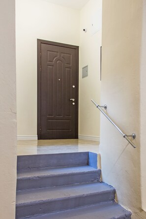 Staircase leads to a dark door with a metal handrail and a small light switch.