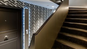 A staircase with a geometric patterned wall and a dark wooden handrail. - Goodge Street II (London)