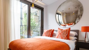 A bedroom with a large bed, a round mirror, and a balcony with a view of buildings. - Goodge Street II (London)