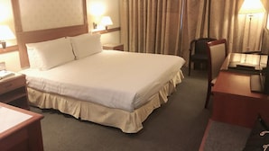 Een hotelkamer met een groot bed, twee nachtkastjes, een bureau, een stoel en een raam met gordijnen.