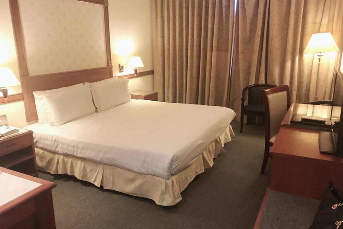 A hotel room with a large bed, two bedside tables, a desk, a chair, and a window with curtains.