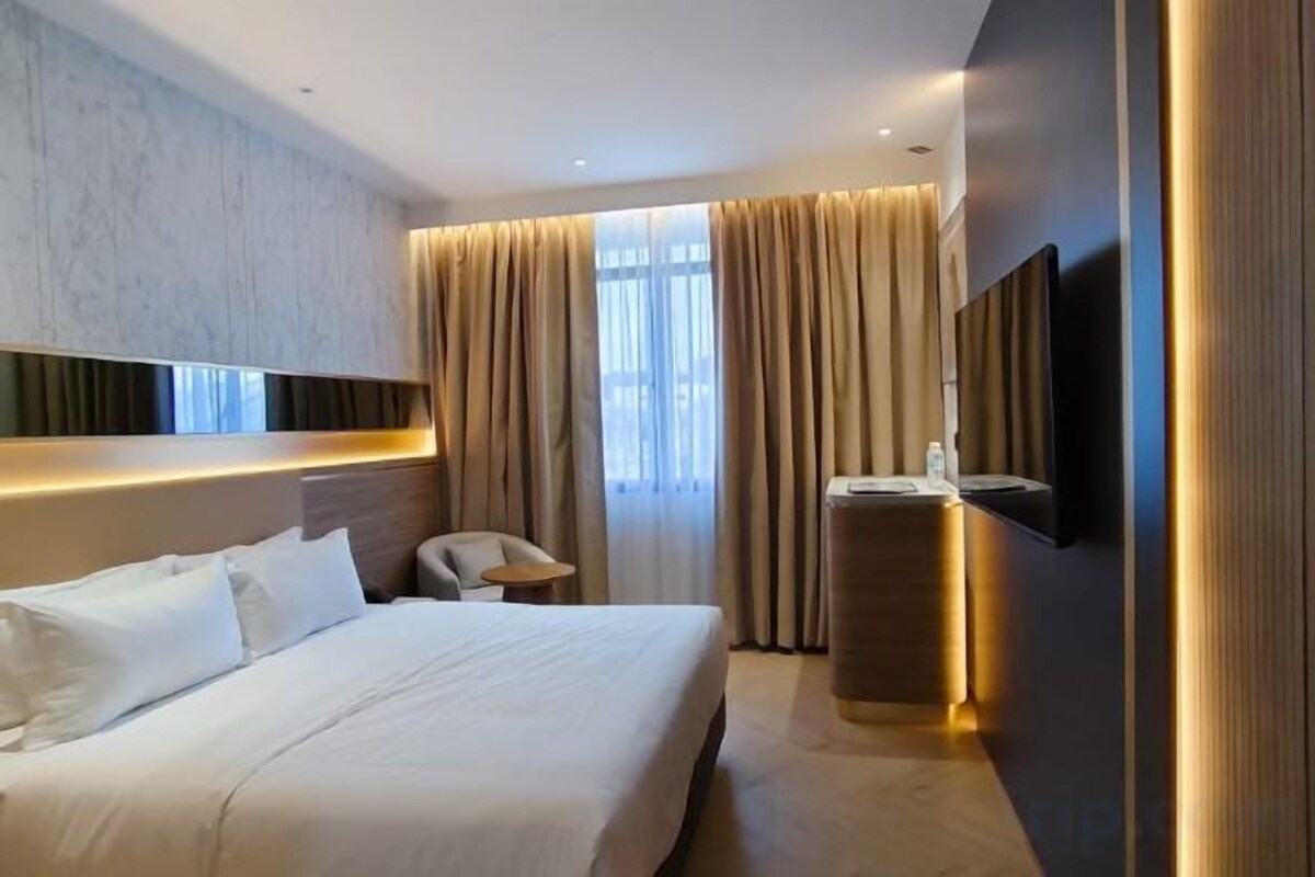 A modern hotel room with a large bed, a desk, a chair, and a TV mounted on the wall.