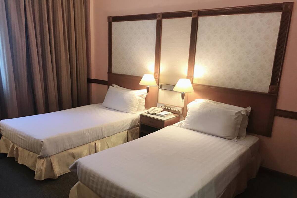 A hotel room with two single beds, a nightstand with a lamp, and a large mirror above the beds.