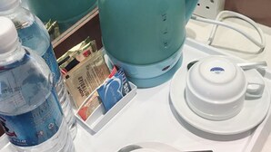 Een kitchenette met een blauwgroene elektrische waterkoker, een witte theepot, een waterfles en een theeservies.