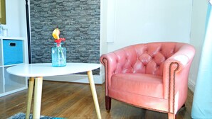 A pink leather armchair with wooden legs, a white table with a glass vase, and a stone wall. - The Kings Head Inn (Warwick)