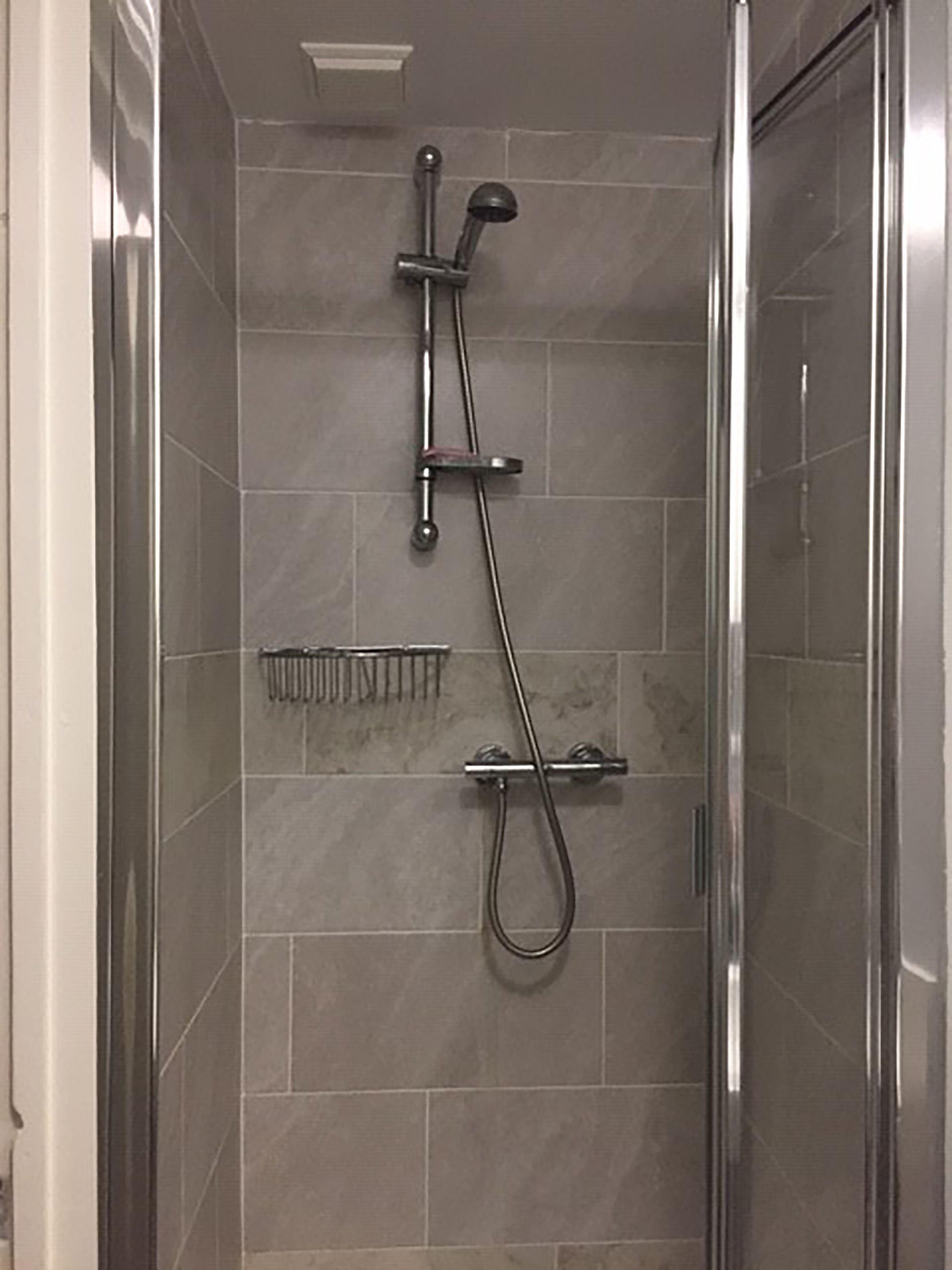 A shower with a handheld showerhead and a fixed showerhead, a small shelf, and a glass shower enclosure.