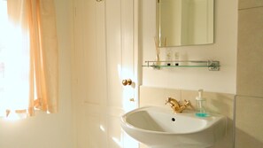 A bathroom with a white sink, gold faucet, and a glass shelf above it.