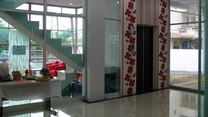 A modern hotel lobby with a staircase, a reception desk, and large windows offering views of the outdoors. - Choke-Set-Thee House (Ayutthaya)