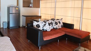 A modern living room with a sofa, a small kitchen area, and a large window. - Choke-Set-Thee House (Ayutthaya)