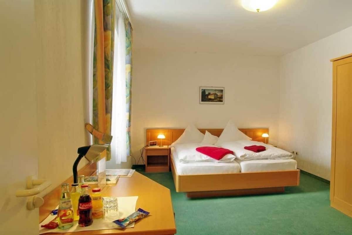 A hotel room with a bed, bedside tables, a desk with toiletries, a wardrobe, and a window with curtains.