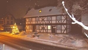 Una casa tradicional d'estructura de fusta i enduint amb estuc, amb el terreny cobert de neu i un arbre de Nadal il·luminat al davant.