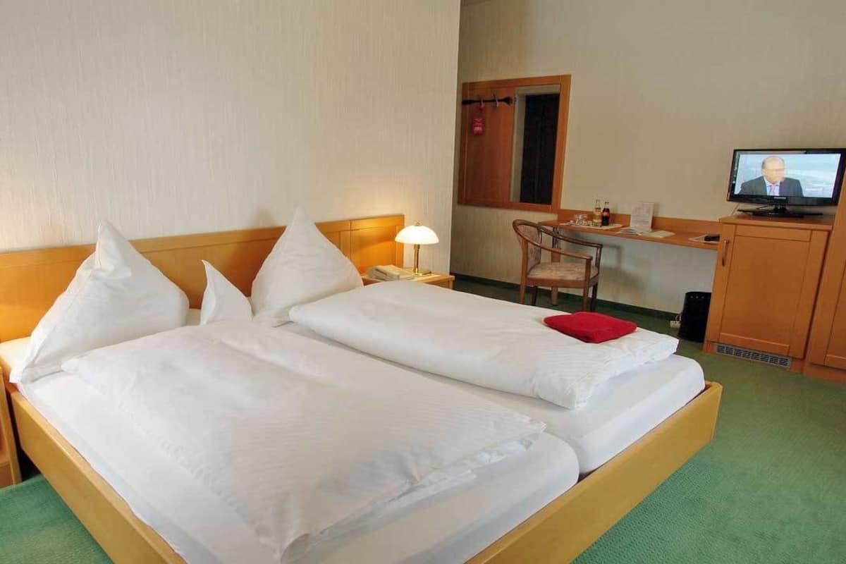 A hotel room with two single beds, a desk, a television, and a chair.