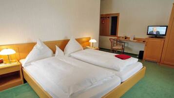 Ein Hotelzimmer mit zwei Einzelbetten, einem Schreibtisch, einem Fernseher und einem Sessel.