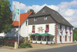 A two-story building with a white facade and a red roof. There is a mural of a horse on the side of the building. - Hotel Restaurant Räuber Lippoldskrug (Alfeld)