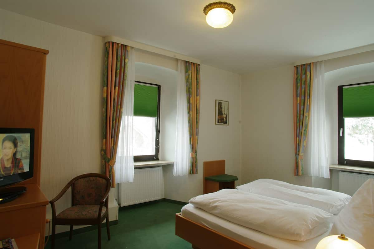 A hotel room with a bed, a chair, a small table, and a television.