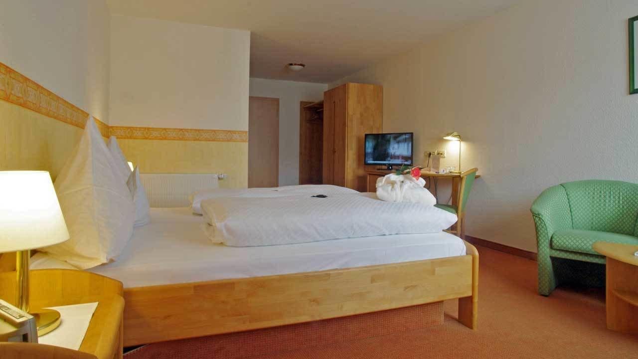 Een hotelkamer met een houten bed, een televisie, een groene fauteuil en een bureau met een lamp.
