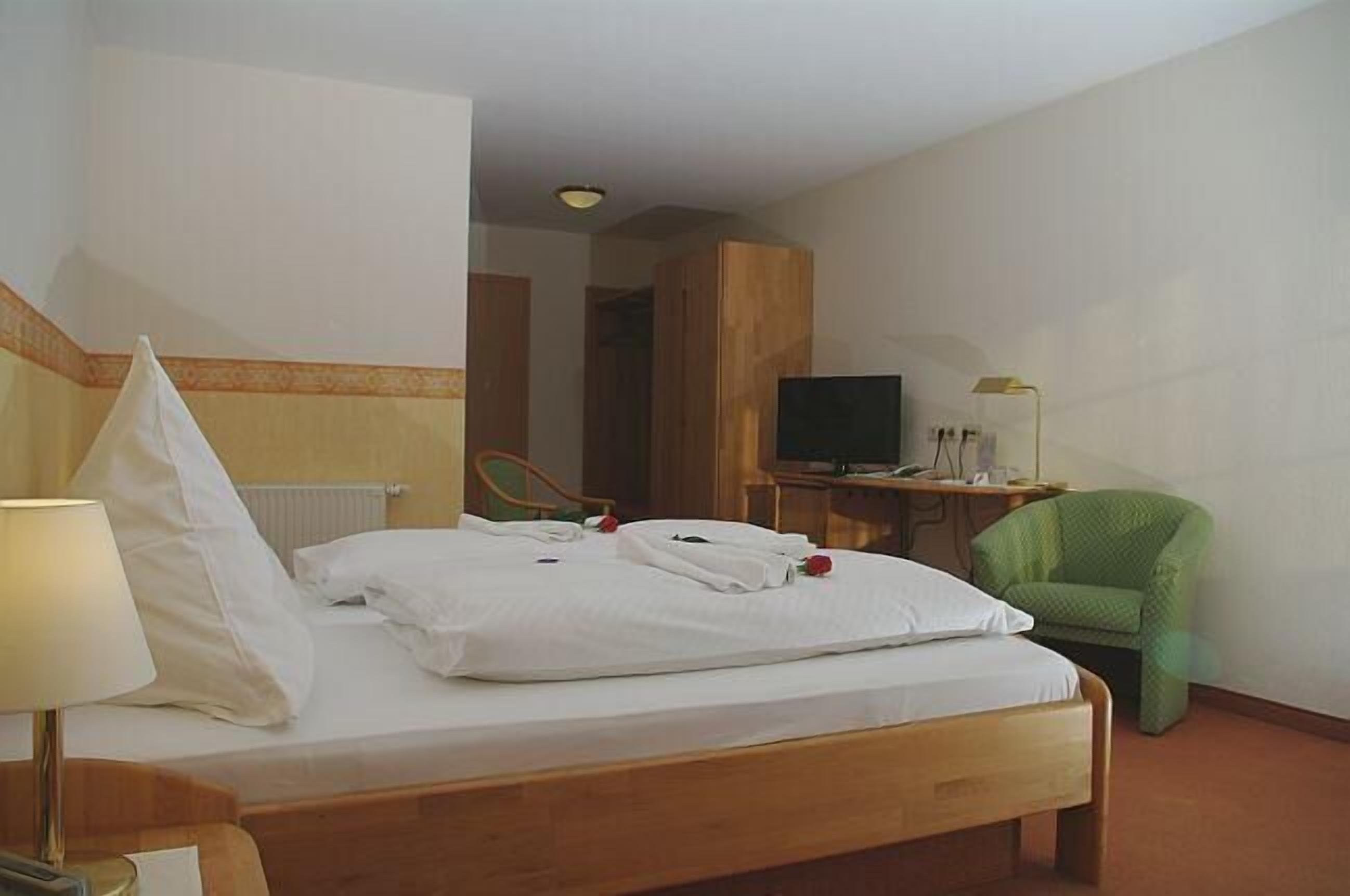 A hotel room with a bed, a television, a desk, and a green chair.