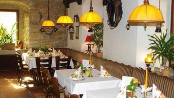 A restaurant with stone walls, tables with white tablecloths, and yellow hanging lamps.