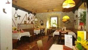 Una zona de menjador rústica amb taules i cadires de fusta, parets de pedra i làmpades penjants.