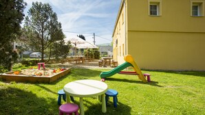 A sunny outdoor area with a playset, a table with stools, and a building in the background. - Penzion u Vyhlídky (Chribska)