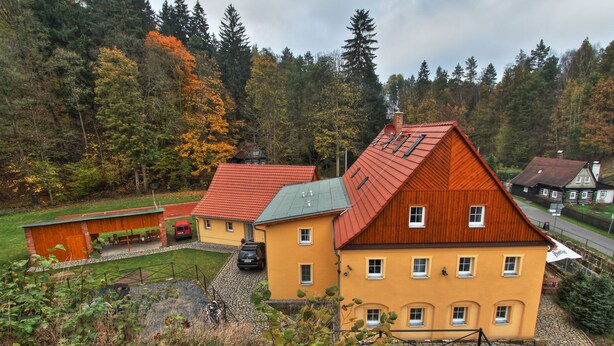 A cluster of houses with red roofs and yellow walls, surrounded by a forested area. - Penzion u Vyhlídky (Chribska)