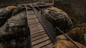 A wooden bridge leading to a viewing platform with a metal railing, overlooking a mountainous landscape. - Penzion u Vyhlídky (Chribska)