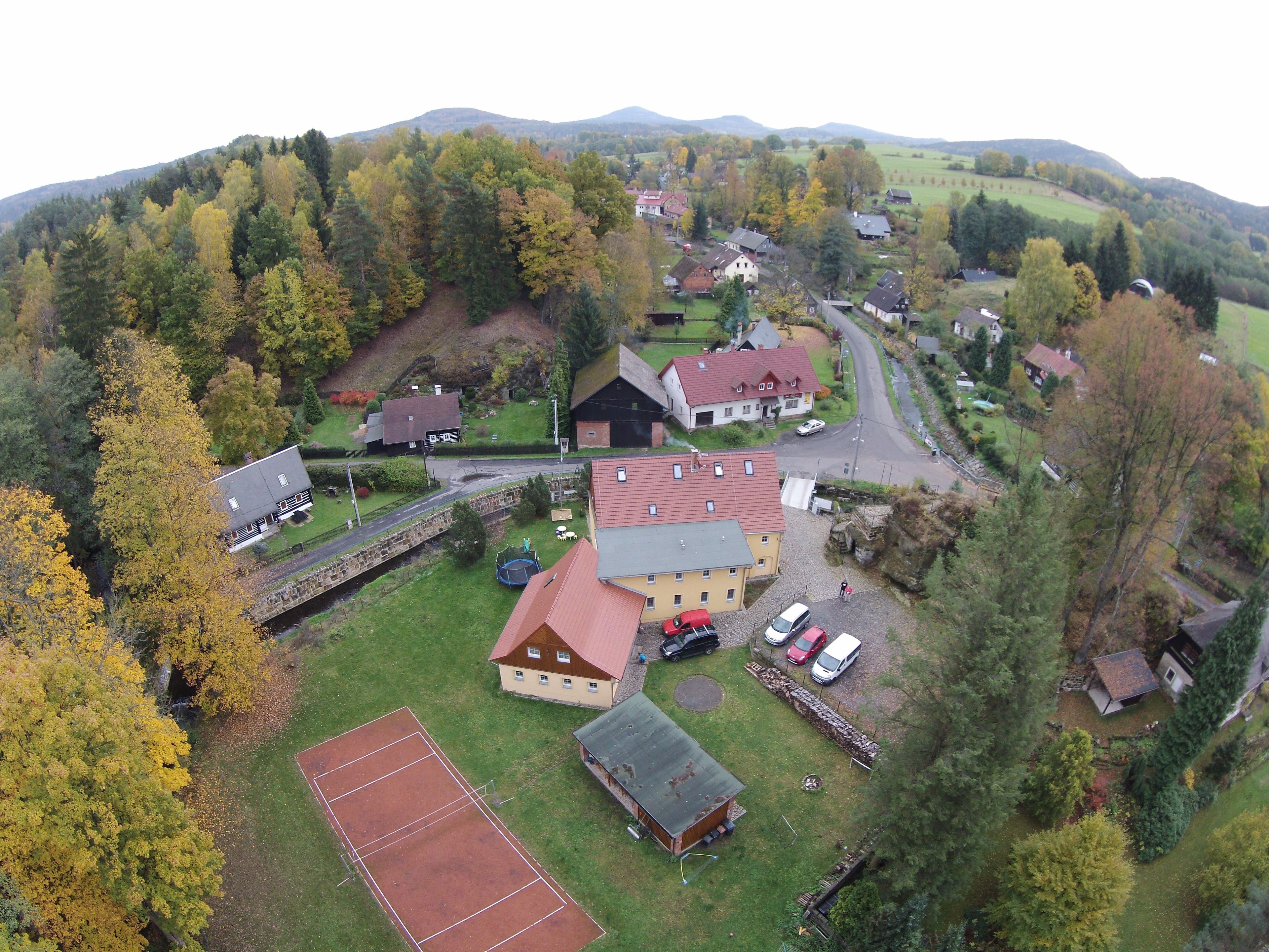 Vista aérea de un pueblo rural con casas, una cancha de tenis y vegetación circundante.