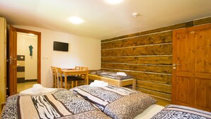 A bedroom with two beds, a wooden wall, a TV, and a desk with chairs. - Penzion u Vyhlídky (Chribska)