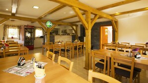 A dining area with wooden tables and chairs, a bar in the background, and a Coca-Cola refrigerator. - Penzion u Vyhlídky (Chribska)