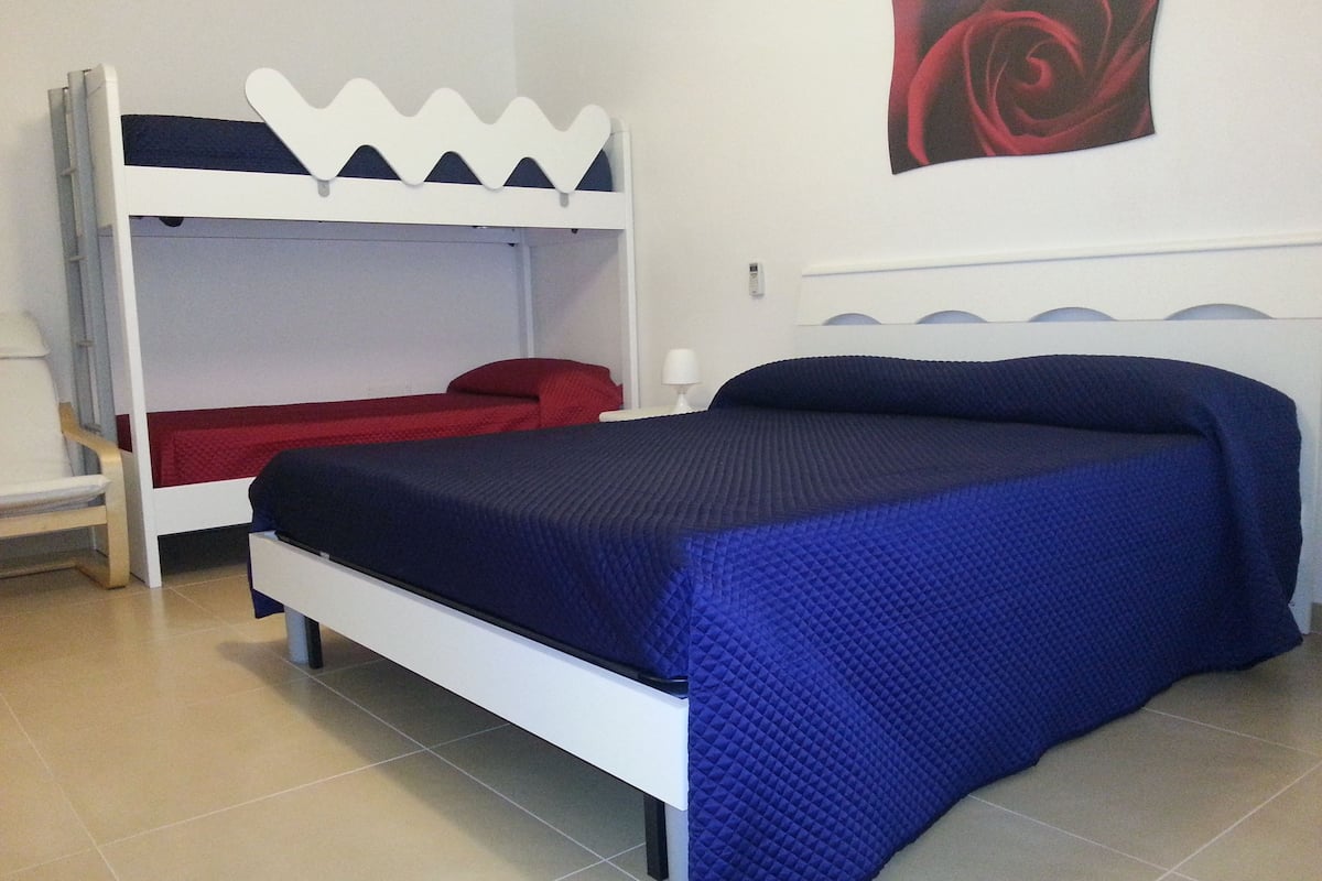 A room with a bunk bed, a single bed, a chair, and a wall art piece.