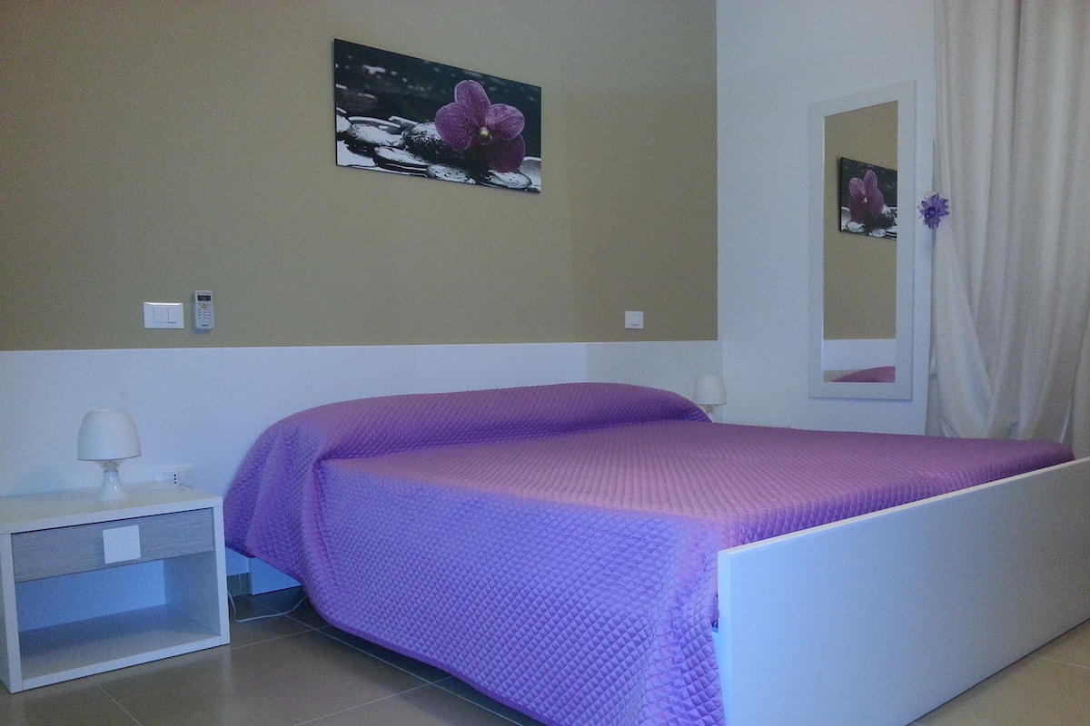 A bedroom with a bed, a nightstand, a wall-mounted phone, and a framed picture.